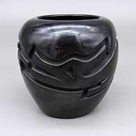 A black jar carved with an avanyu design around the body