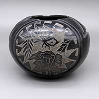 A black bowl with a sgraffito hummingbird and flower design with a carved geometric design
