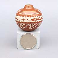 A miniature red jar painted in white with an avanyu and geometric design