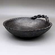 Micaceous black bowl with a braided handle, indentations around rim, and a corrugated bottom
 by Unknown of Taos