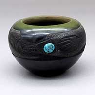 A small, green, black and micaceous black bowl with a sgraffito avanyu design and a turquoise for its eye
 by Russell Sanchez of San Ildefonso