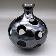 A polished black jar with a flared neck and geometric design of circular cutouts around the body
 by Lucie Tete of Mata Ortiz and Casas Grandes