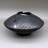 A black-on-black jar with a geometric cut opening, an indented texture, and a painted cuadrillos and geometric design