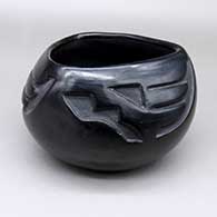 A black bowl with a triangular opening and carved with a geometric design