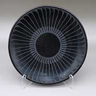 A black-on-black plate with a painted ring-of-feathers geometric design