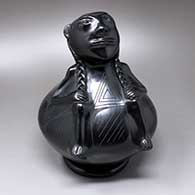 A black human effigy on a polished black jar decorated with a matte black geometric design