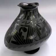 An oval black-on-glossy black jar with a rolled square lip and painted geometric design