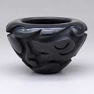 A small black bowl carved with an avanyu and geometric design around the outside