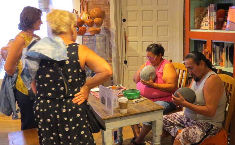 Paula Estevan painting a jar and Robert Kasero Sr. burnishing a seed pot