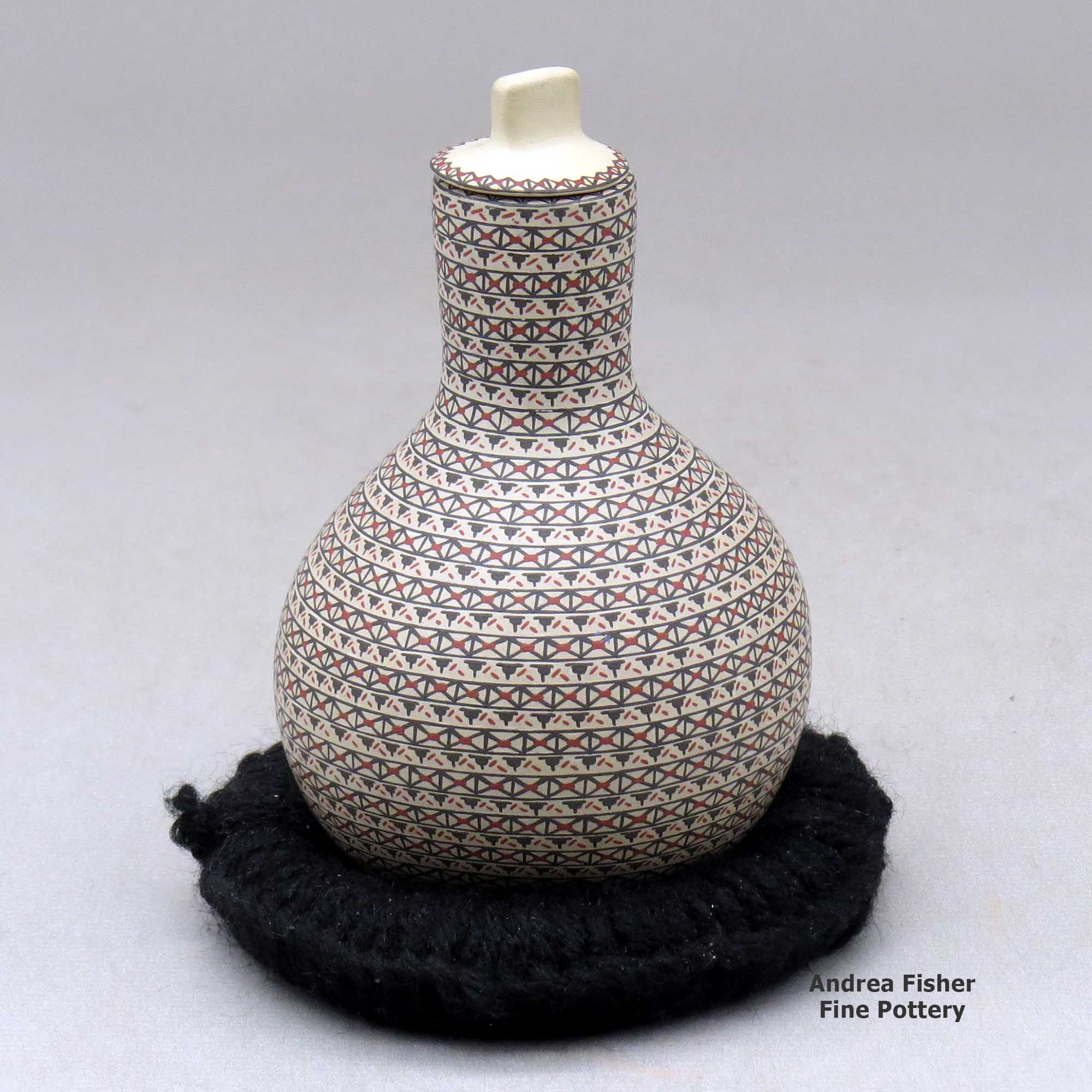 Click or tap to see a larger view A small tall necked lidded jar decorated with a tiny lines geometric design made by Karla Lopez Cota of Mata Ortiz and Casas Grandes