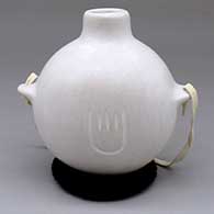A white canteen with nub handles decorated with a carved bear paw
 by Andrew Padilla of Laguna