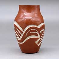 A red vase carved with an avanyu and geometric design around the body, click or tap to see a larger version