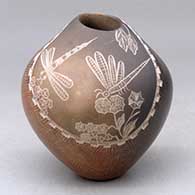 A brown jar with an organic opening and a lightly carved necklace around a sgraffito dragonfly, leaf, flower and plant design
 by Bernice Naranjo of Taos