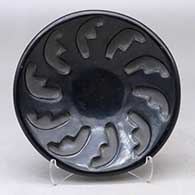 A shallow black bowl carved with a ring of feathers design
 by Belen Tapia of Santa Clara