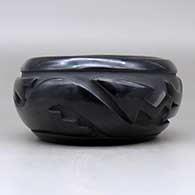 An oval black bowl polished inside and carved around the outside with an avanyu and geometric design, click or tap to see a larger version