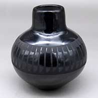A black on black jar with a raised rim and decorated around the shoulder with a band of feathers design
 by Helen Gutierrez of San Ildefonso