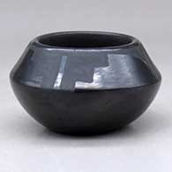 A small black on black bowl decorated above the shoulder with a four panel geometric design
 by Rose Gonzales of San Ildefonso