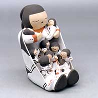 A sitting grandmother storyteller with a twisted braid, wearing a manta and holding eight children
 by Chris Teller of Isleta