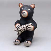 A sitting black bear figure holding a fish
 by M Janice Ortiz of Cochiti