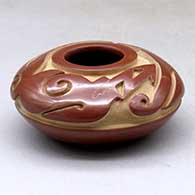 A small red seed pot carved with an avanyu and geometric design above the shoulder
 by Sergio Youngblood of Santa Clara