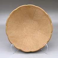A shallow buff bowl with a notched rim and decorated on the inside with a lightly carved and golden micaceous painted ancient rock art design
 by Tomasita Reyes Montoya of Ohkay Owingeh