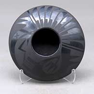 A black on black bowl with a black micaceous base and decorated above the shoulder with an avanyu and feather geometric design
 by Marvin and Frances Martinez of San Ildefonso