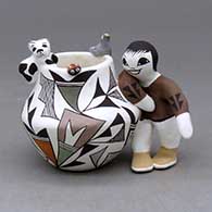 A small polychrome jar with a boy on the side, a cat, lady bug and bird applique on the rim, all decorated with a geometric design
 by Judy Lewis of Acoma