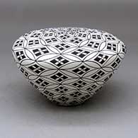 A black on white seed pot decorated with a pumpkin seed snowflake and geometric design
 by Cletus Victorino of Acoma