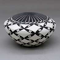 A black on white seed pot decorated with a feather and pumpkin seed snowflake geometric design
 by Cletus Victorino of Acoma