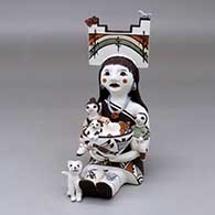 A sitting grandmother storyteller figure wearing a tablito and holding two children with a cat, butterfly, birds, lady bugs and a pot
 by Judy Lewis of Acoma