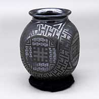 A black on glossy black jar with a flared rim and flat sides, all decorated with a four panel tiny square and geometric design around the body
 by Eligio Ortiz of Mata Ortiz and Casas Grandes