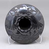 A black seed pot with a notched rim and decorated above the shoulder with a sgraffito hummingbird, flower, vine and berry design
 by Lupita Quezada of Mata Ortiz and Casas Grandes