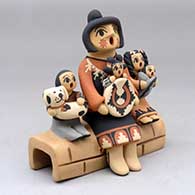 A grandmother storyteller figure sitting on a stone wall with four children, a puppy and a welcome basket
 by Chrislyn Fragua of Jemez