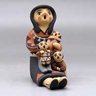 A sitting grandmother storyteller figure holding three children and a drum, click or tap to see a larger version