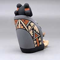 A sitting grandmother storyteller figure wearing a manta and holding four children, a pot and an ear of corn, click or tap to see a larger version