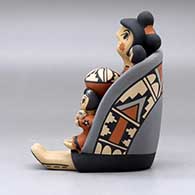 A sitting grandmother storyteller figure wearing a manta and holding four children, a pot and an ear of corn, click or tap to see a larger version