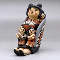 A sitting grandmother storyteller figure wearing a manta and holding four children, a pot and an ear of corn, click or tap to see a larger version