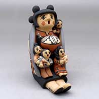 A sitting grandmother storyteller figure wearing a manta and holding four children, a pot and an ear of corn
 by Chrislyn Fragua of Jemez