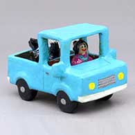 A polychrome pickup truck with a dog in the back and a woman driving
 by Elizabeth Manygoats of Dineh