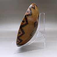 A shallow polychrome bowl decorated with a sgraffito and painted yeibichai, sun shield, feather and geometric design, click or tap to see a larger version