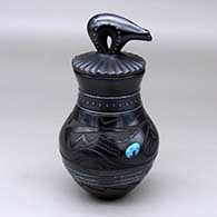 A lidded black jar with an inlaid turquoise, sgraffito avanyu and geometric design, and bands of inlaid hematite heishi beads and single stones with a sculpted bear on the lid
 by Russell Sanchez of San Ildefonso