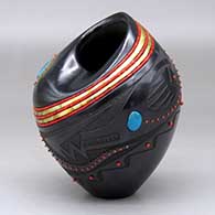 A black jar with an organic opening and decorated with a sgraffito avanyu and geometric design and bands of inlaid beads and stones
 by Russell Sanchez of San Ildefonso