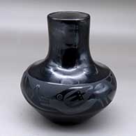 A black on black tall neck jar decorated around the shoulder with an avanyu and geometric design
 by Santana Martinez of San Ildefonso