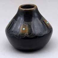 A small black jar with sienna spots, four inlaid stones and decorated with a sgraffito feather and geometric design above the shoulder
 by Barbara Gonzales of San Ildefonso