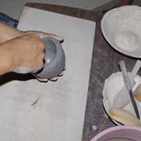 Using a piece of a gourd to work the clay on the inside