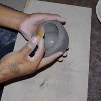 Using a piece of gourd to work the clay outwards